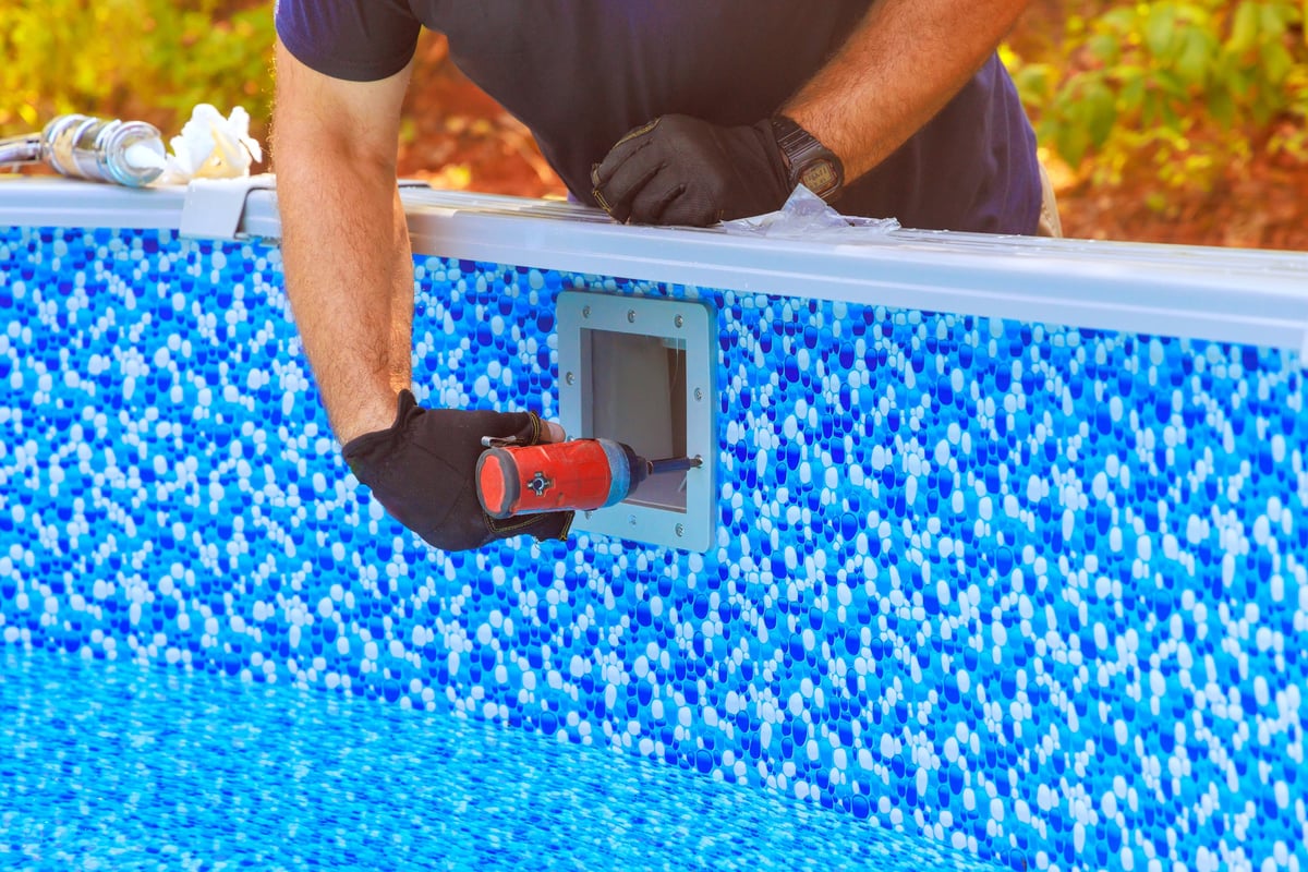 Worker installing pool filtration equipment by blue swimming pool